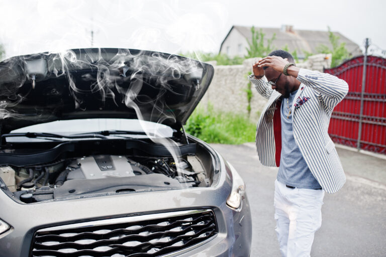 car with open hood with the engine in smokes while the driver is standing on the side frustrated