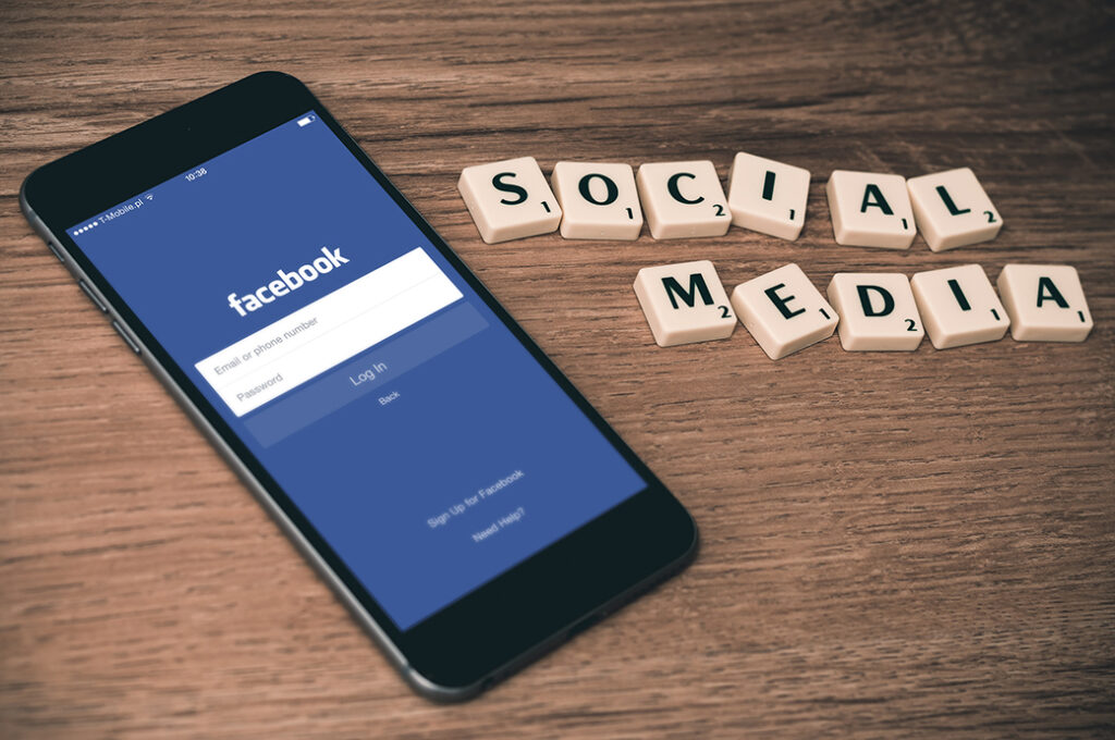 phone with Facebook app open beside Scrabble tiles that spell "social media"