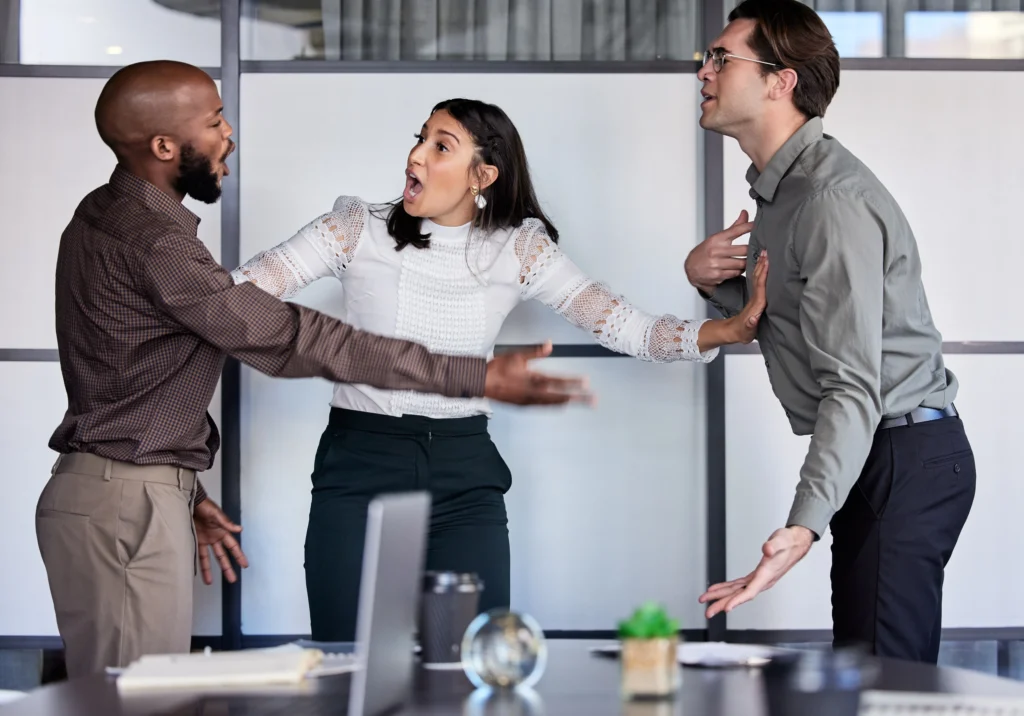 A tense discussion occurs between three professionals in a modern office setting, expressing disagreement and gesturing with hands.