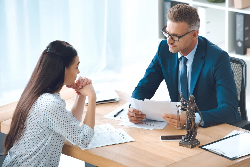 A business meeting at a wooden table, with documents and a statue of Lady Justice, hinting at legal discussions.