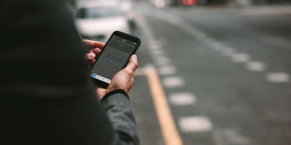 Person holding a smartphone on the side of a road in California, likely using a rideshare app to request a ride.