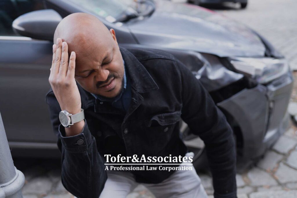 A man in pain next to a wrecked car