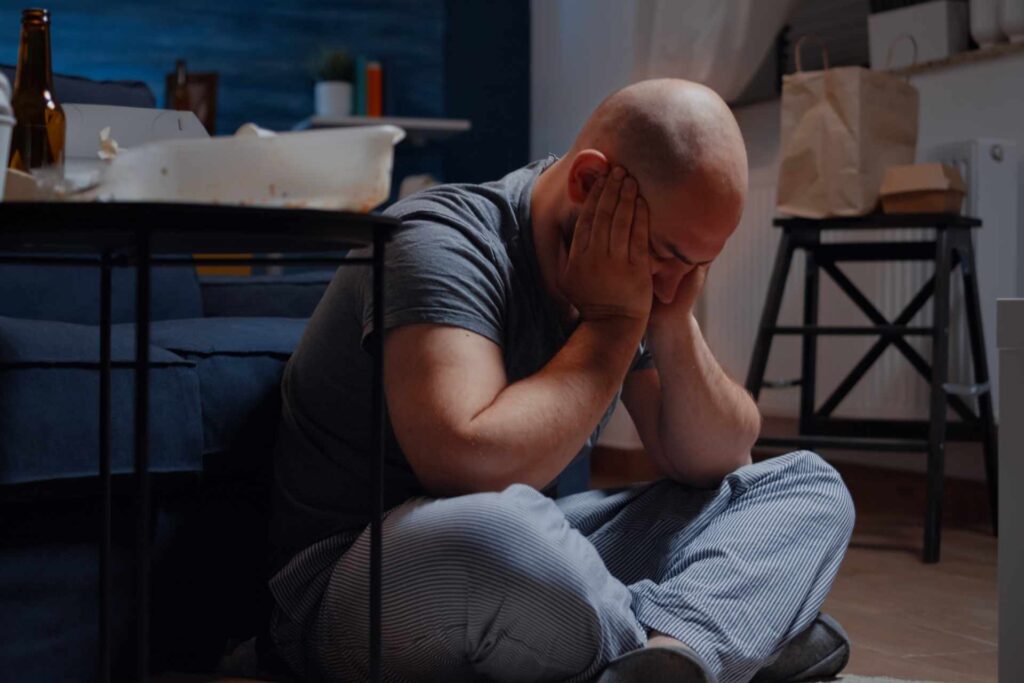 Man sitting on the floor with his head in his hands, visibly distressed, illustrating emotional pain, stress, and suffering