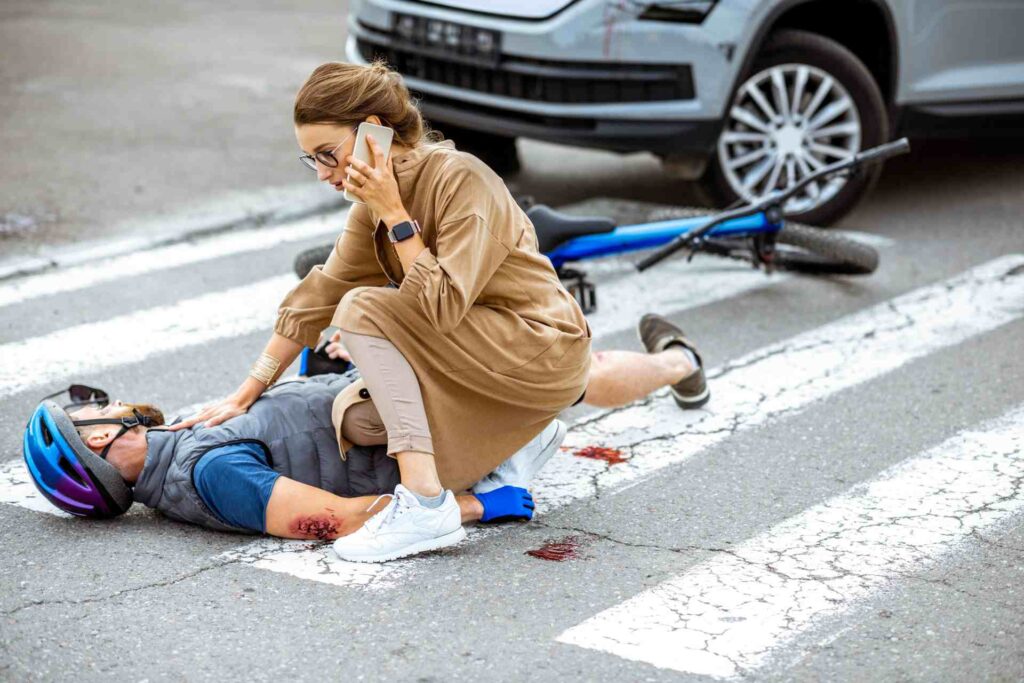 Woman calling for help while attending to an injured cyclist lying on a crosswalk after a bike accident
