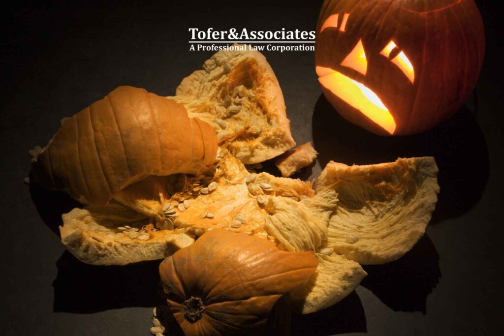 Broken pumpkin pieces with a carved pumpkin face in the background after a halloweeen accident