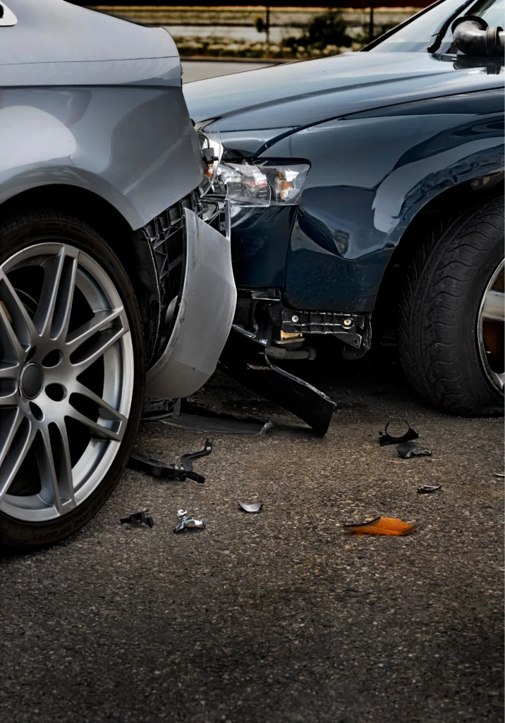 Two cars, one silver and one dark blue, are damaged after a collision, with debris scattered on the road.