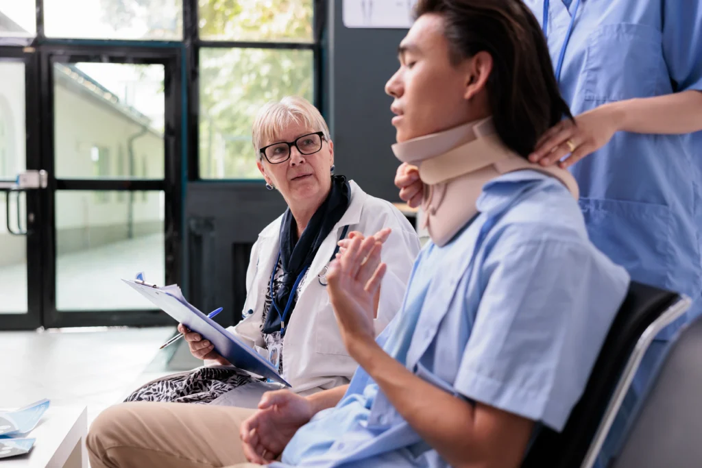 A medical professional consults with a patient wearing a neck brace, seated in a well-lit clinic with large windows.