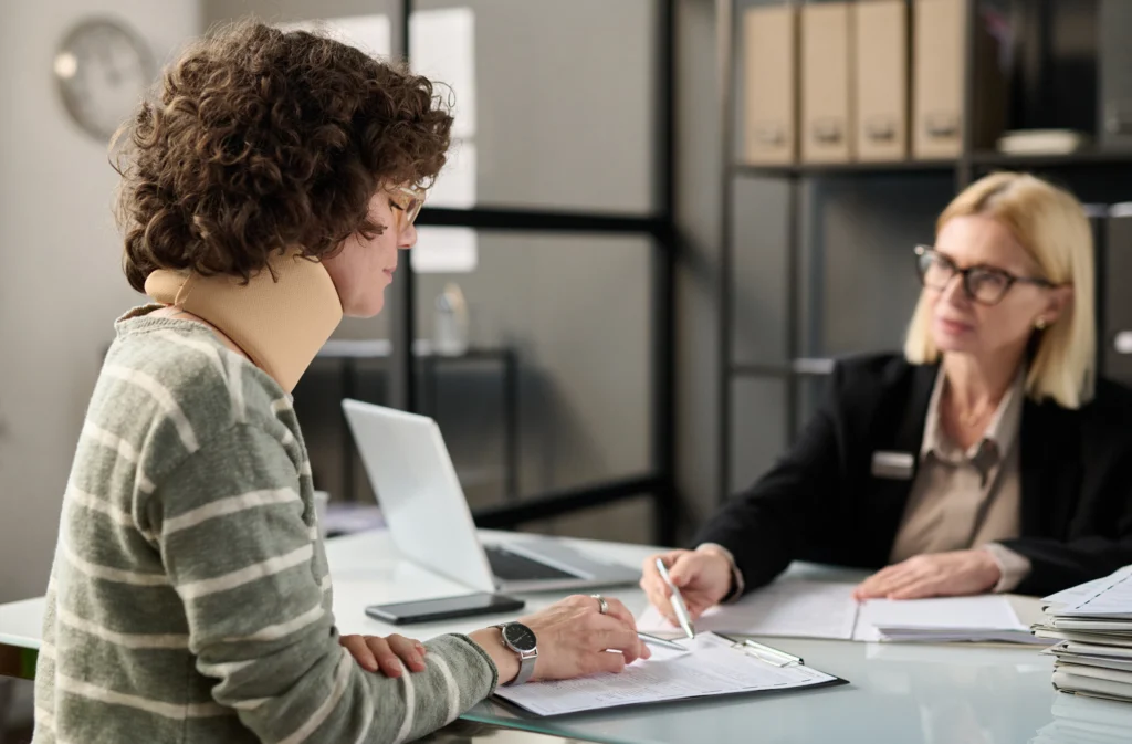 A person with curly hair sits at a table, engaged in a discussion while reviewing papers with another individual.
