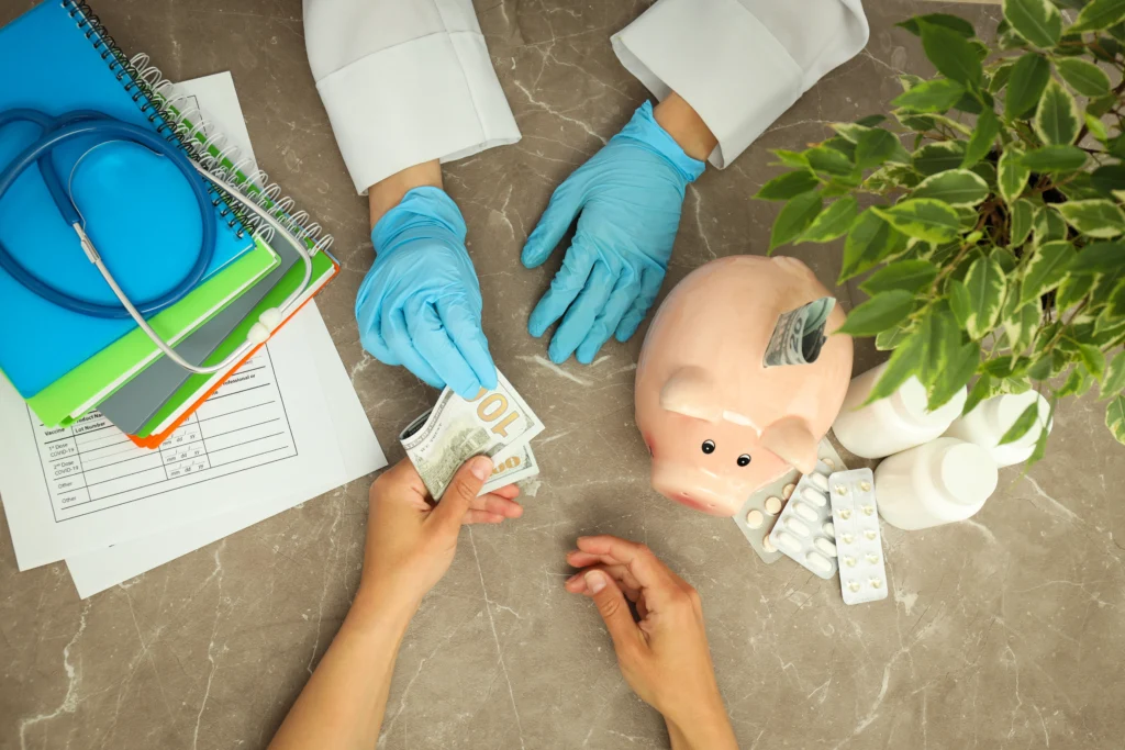 A healthcare professional in gloves exchanges cash with a patient, surrounded by medical supplies, papers, and a piggy bank.
