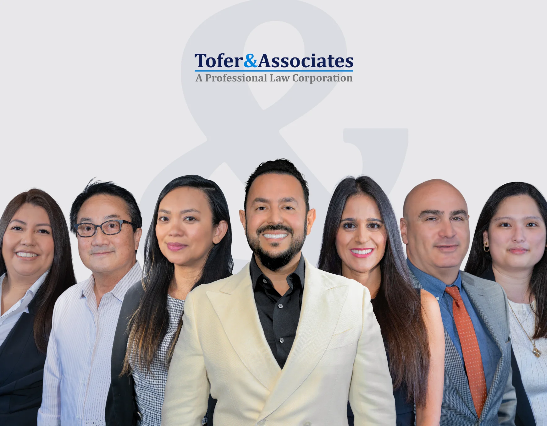 A group of professionals lawyers standing together, representing the law firm Tofer & Associates, against a neutral backdrop.