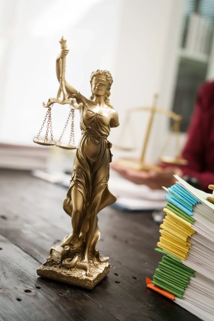 A golden statue of Lady Justice holding scales, surrounded by stacked colored file folders on a wooden table.
