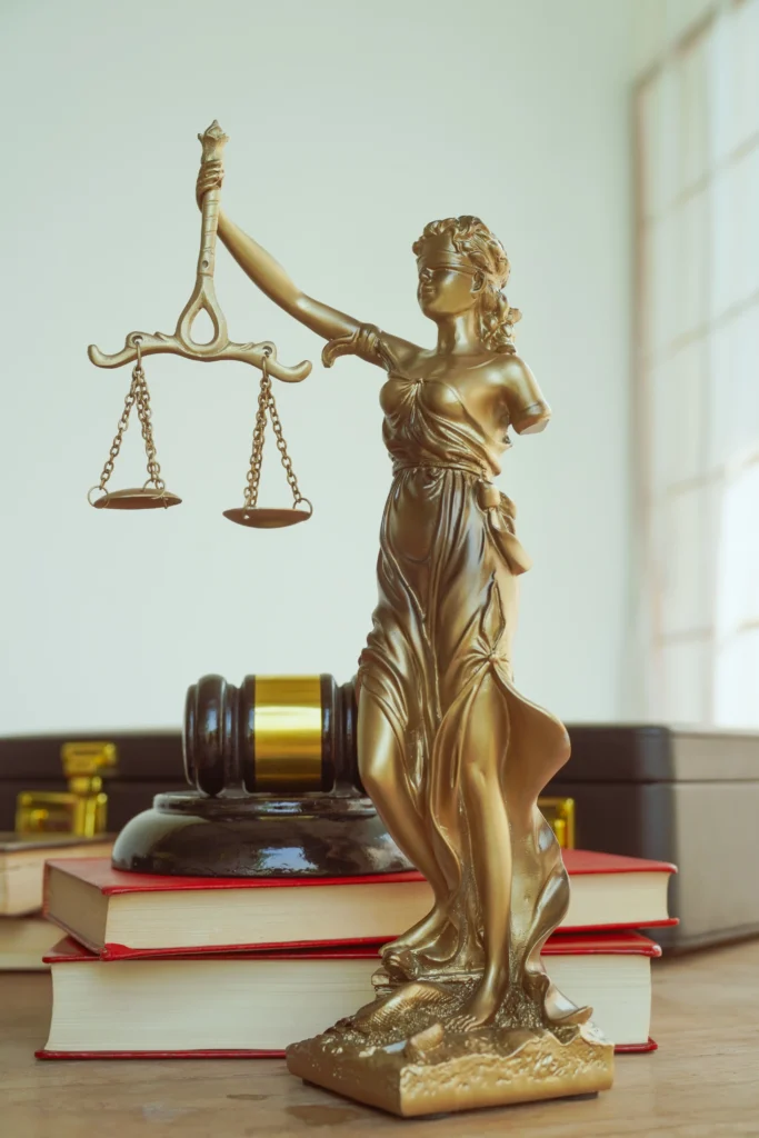 A golden statue of Lady Justice holding scales, beside a gavel and stacked law books, symbolizing legal practice and fairness.