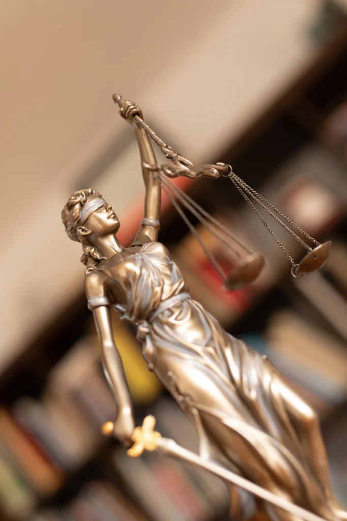A bronze statue of Lady Justice holding scales and a sword, symbolizing fairness and law, set against a blurred background of books.