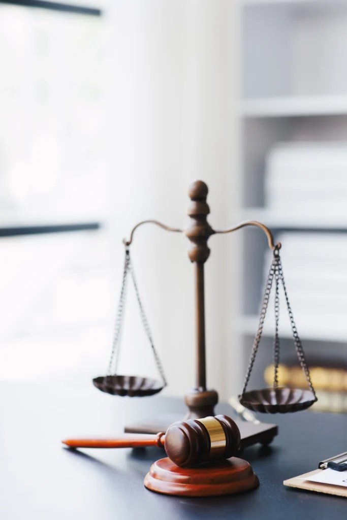 A wooden gavel and balance scales on a desk, symbolizing justice and law in a bright office environment.