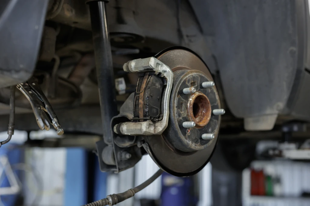 Close-up of a car brake assembly with visible rotor, caliper, and brake pads. The image conveys a mechanical, technical tone in an auto repair setting.